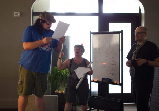 person reading from paper as two others watch