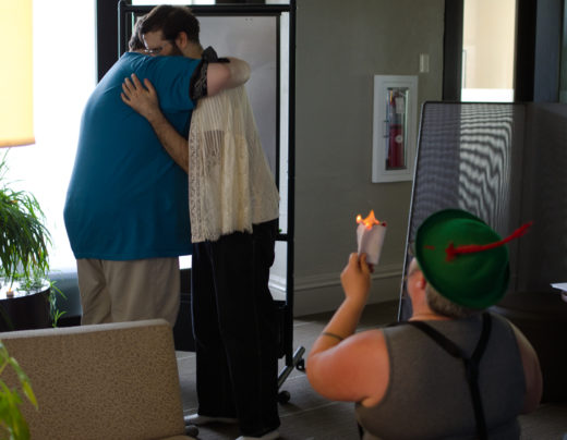 two people embrace as third person in foreground burns a paper document