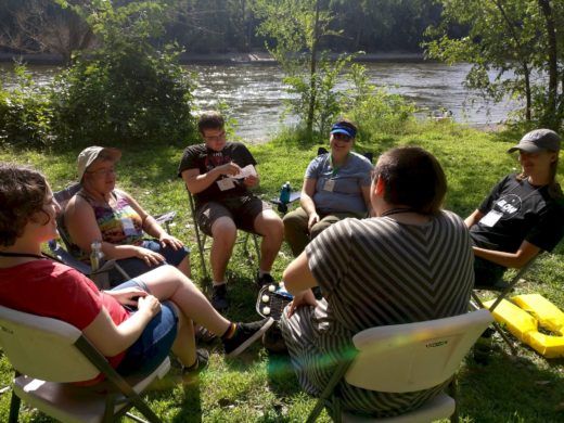 six people seated in circle on shoreline