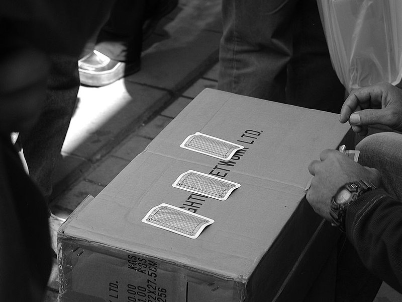 A black-and-white photo of a game of three-card monty being played on a cardboard box