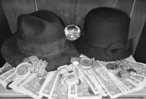 A black-and-white photo of a pair of old-fashioned felt hats with an spread of cash and other valuables