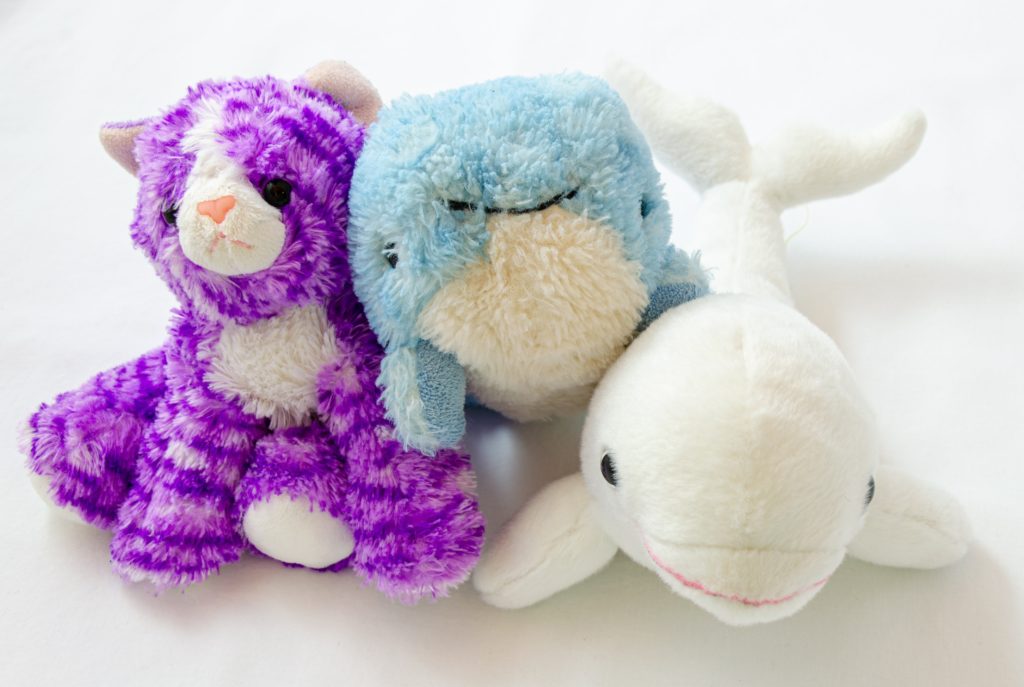 Three stuffed animals rest next to one another: A purple tiger, a sky blue whale, and a white porpoise.