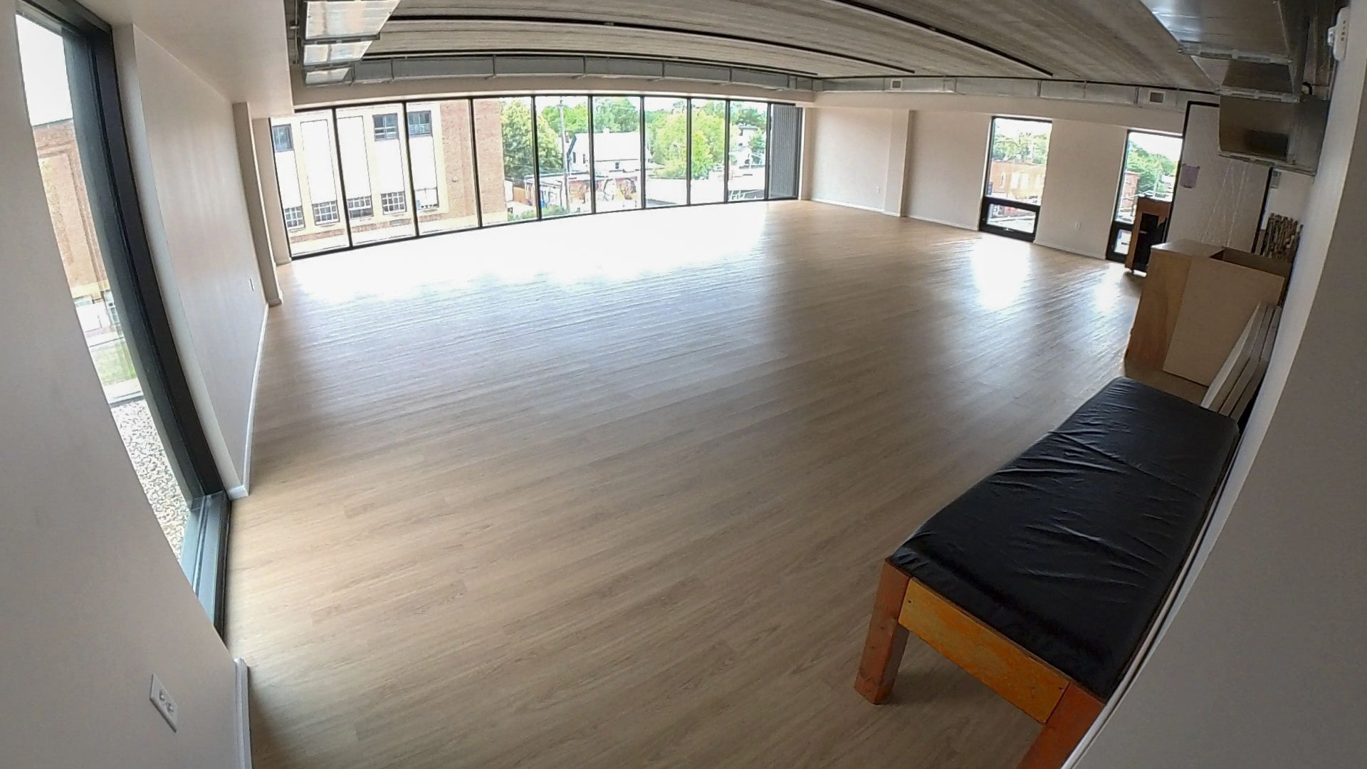 A wide angle view of a wooden floored dance studio with floor to ceiling windows along one wall.