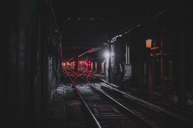 A New York subway tunnel is illuminated by glaring red lights. It is dark and deserted.